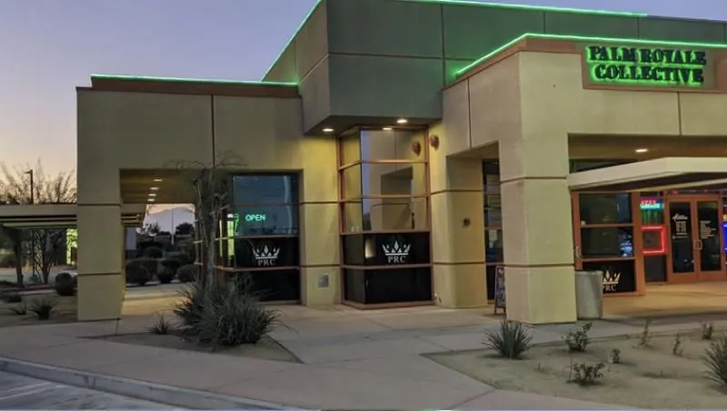 A Palm Royale Collective storefront at dusk with green neon trim and PRC crown logos in the windows